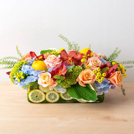 This bright and cheery centerpiece is ideal for any summer gathering. In a transparent glass container, fresh summer novelty flowers are complemented with fresh lemon slices.