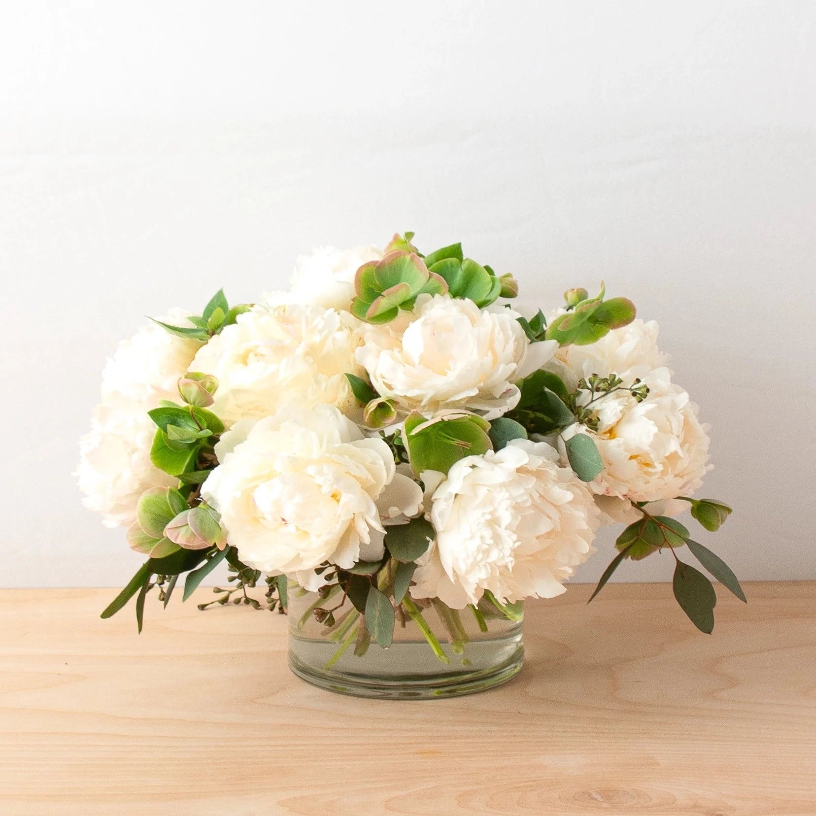 Our Classy Peonies arrangement features a luscious vase of Cream peonies and is made with luxury, richness, and elegance. Hellebores and seeded eucalyptus are accented in a clear glass vase.