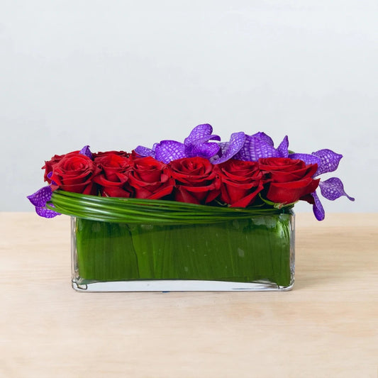 This arrangement of twelve red roses and purple orchids is elegantly put in a glass vase, creating a fresh spin on the classic dozen red roses and the ideal bouquet to demonstrate your unending love.