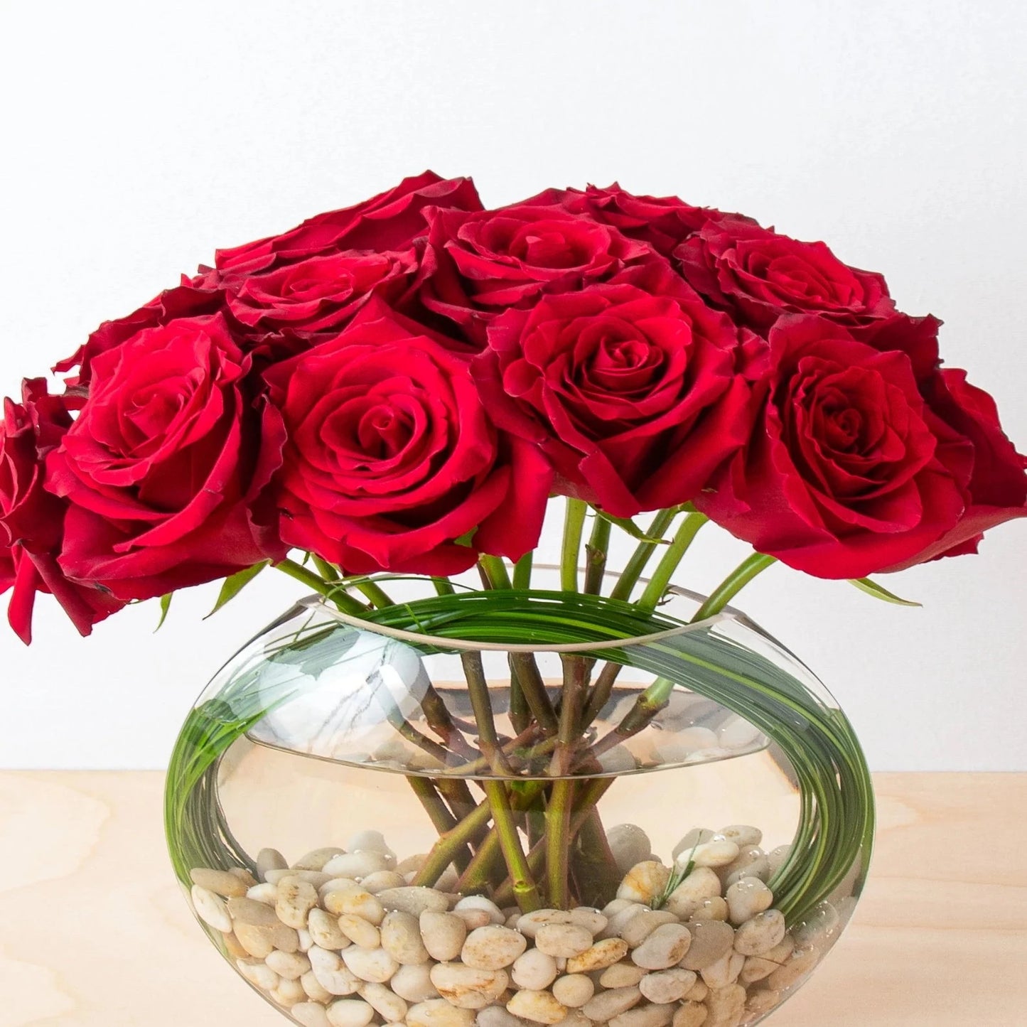 Red roses, but with a contemporary twist. Red novelty Explorer flowers in a new and trendy style. In a flat fishbowl, natural boulders and bear grass are accented.  NOTE: Pure white rocks will be used in place of natural rocks (as shown).